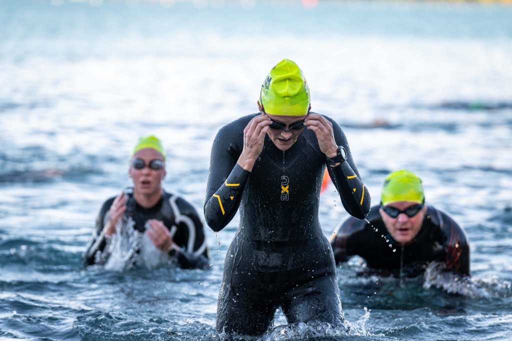 Three swimmers reaching the end and catching their breath as they stand up to leave the water.