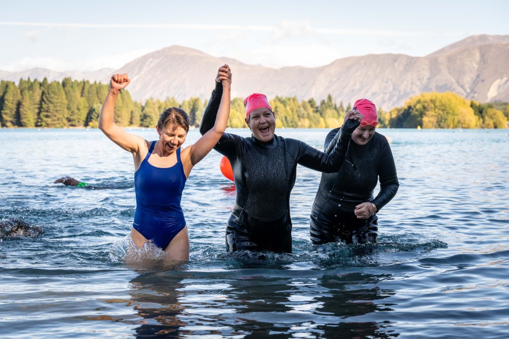 Three women competitors reaching the finish line together with hands held triumphantly in the air
